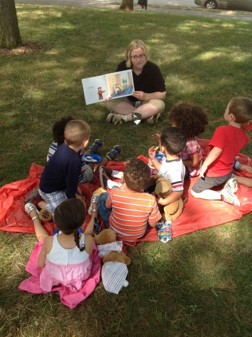 Day Nursery Indianapolis Federal Center students listening to story while in the park for teddy bear picnic
